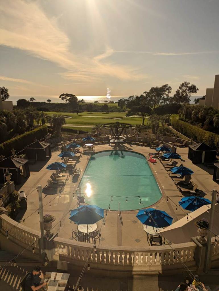 lovely photo looking out over a hotel pool, with a golf course in the background, and the ocean beyond that